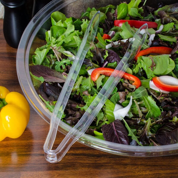 Clear plastic tongs serving salad in a bowl.