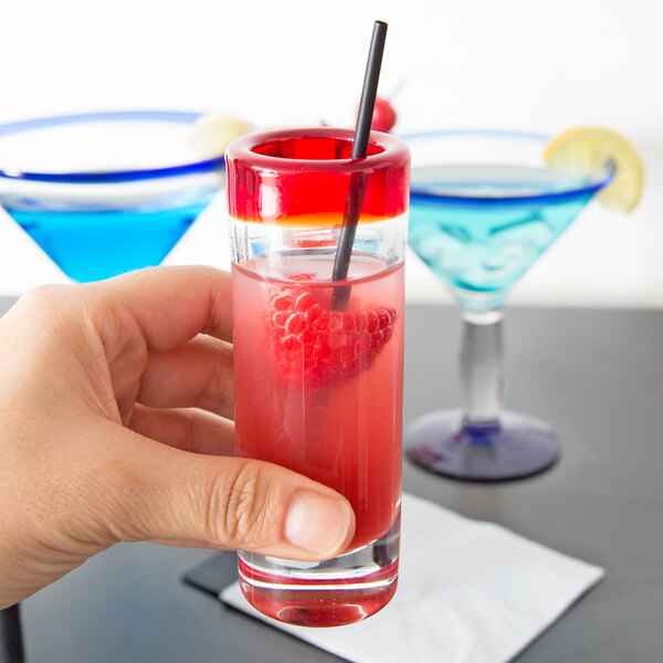 A hand holding a Libbey shooter glass filled with red liquid.