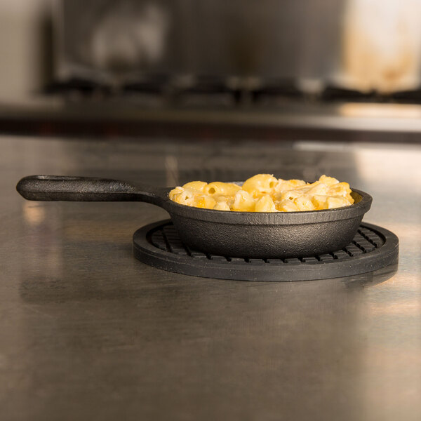 An American Metalcraft black silicone trivet holding a pan of macaroni and cheese on a stove.