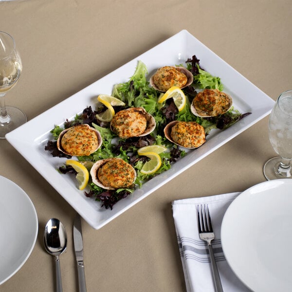A white rectangular melamine serving platter with a plate of clams and lemon wedges.