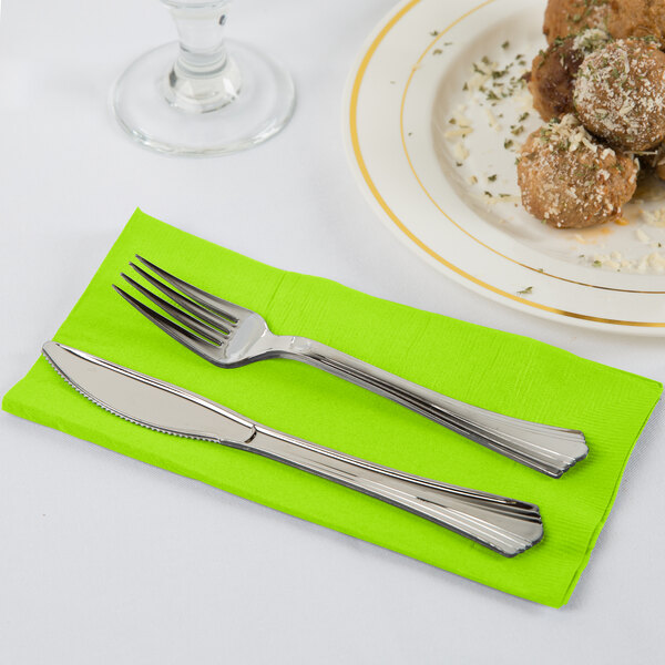 A knife and fork on a lime green Creative Converting paper napkin next to a plate of food.