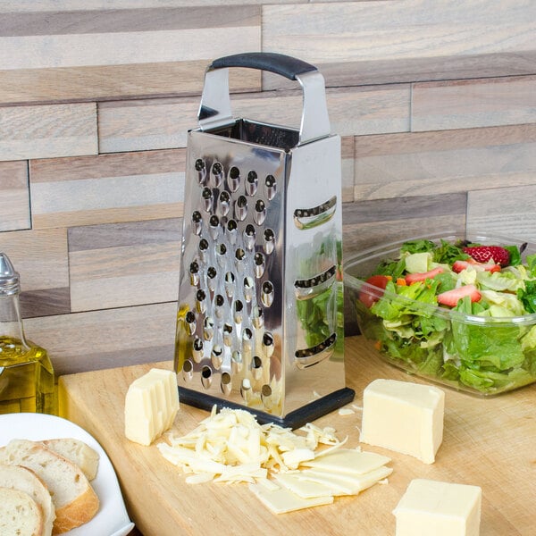 A Tablecraft stainless steel box grater grating cheese and vegetables on a cutting board.