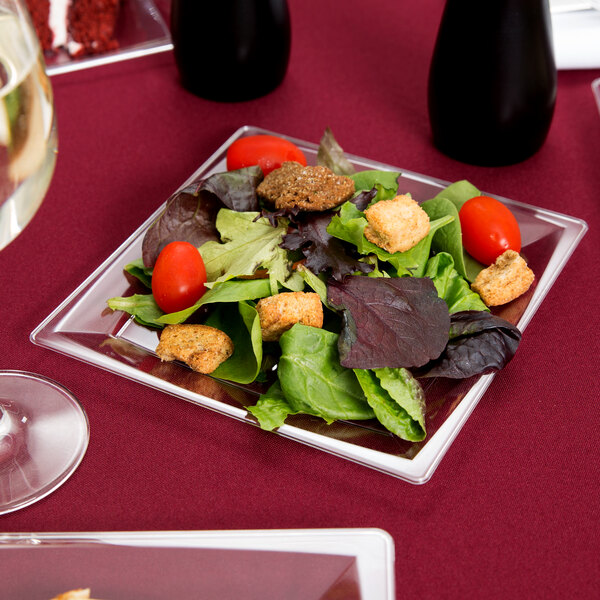 A WNA Comet clear square plastic salad plate with salad on a table.