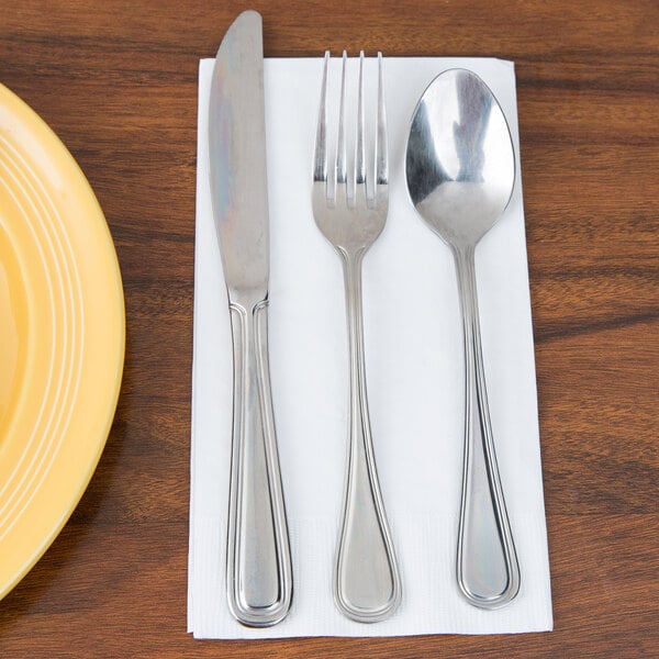 A white Creative Converting guest towel with silverware on a yellow plate.