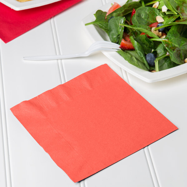 A coral orange luncheon napkin with a fork on a plate of salad.