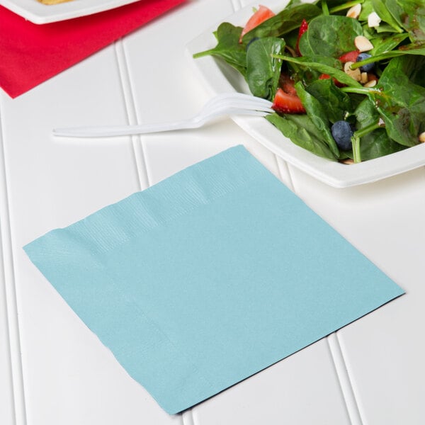 A pastel blue luncheon napkin with a fork on a plate of salad.