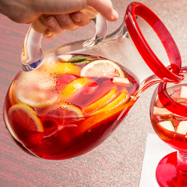 A hand pouring a Libbey Aruba pitcher of red liquid with fruit slices.