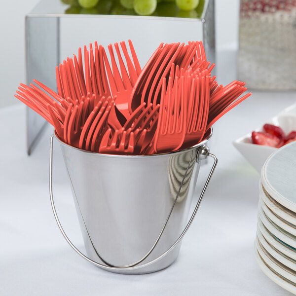 A bucket of coral orange plastic forks on a white background.