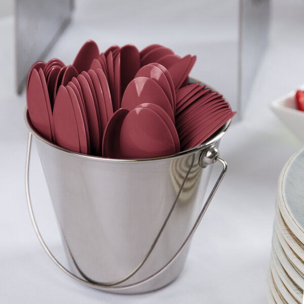 A bucket filled with burgundy plastic spoons and forks.