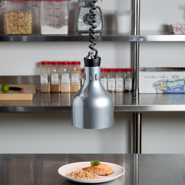 A plate of food on a stainless steel counter heated by a silver Cres Cor infrared bulb.