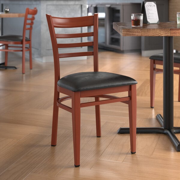 A Lancaster Table & Seating metal ladder back chair with mahogany wood grain finish and black vinyl seat.