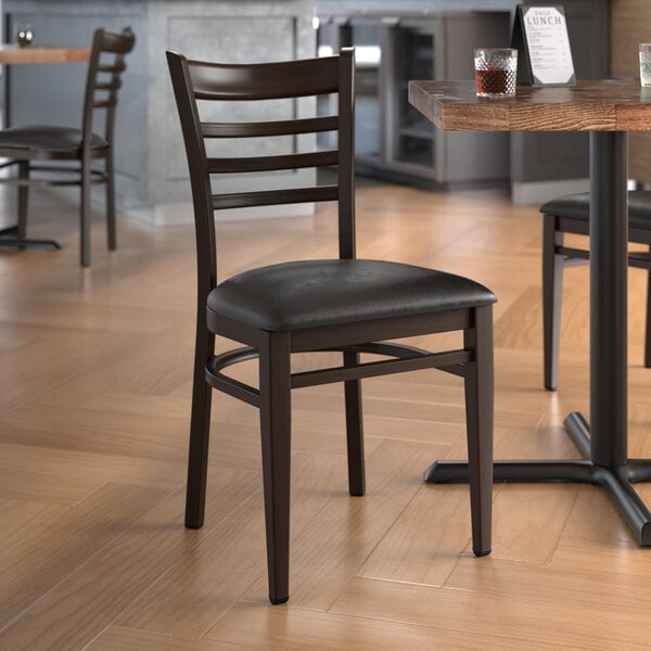 A Lancaster Table & Seating Spartan Series metal ladder back chair with dark walnut wood grain finish and black vinyl seat.