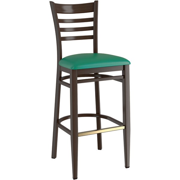 A Lancaster Table & Seating metal ladder back bar stool with dark walnut wood grain finish and green vinyl seat.