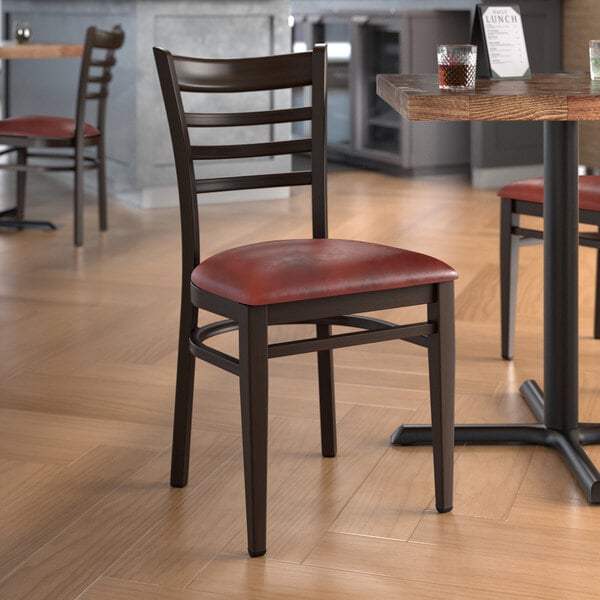 A Lancaster Table & Seating metal ladder back chair with dark walnut wood grain and burgundy vinyl seat in a restaurant.