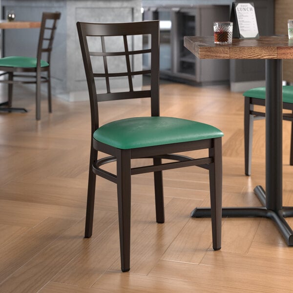 A Lancaster Table & Seating Spartan Series metal window back chair with dark walnut wood grain finish and green vinyl seat.