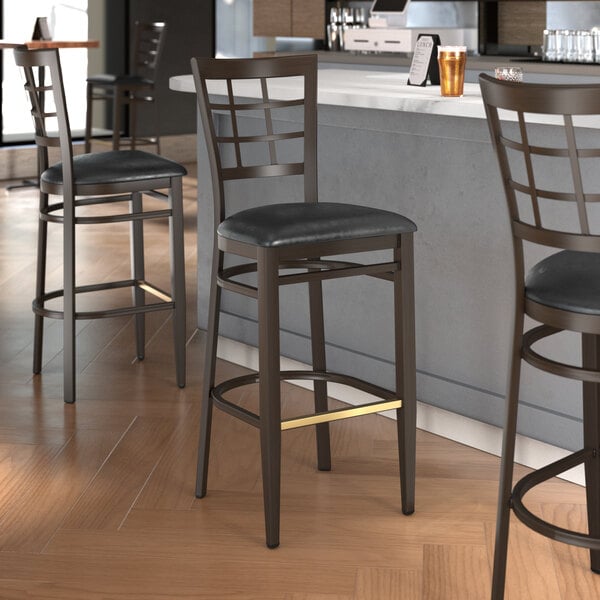 A Lancaster Table & Seating bar stool with black vinyl seat and dark walnut wood grain finish on a metal frame.