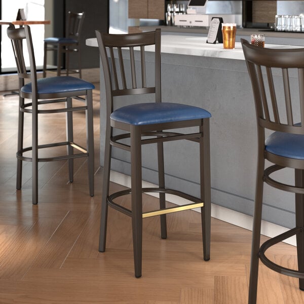Three Lancaster Table & Seating Spartan Series metal slat back bar stools with navy vinyl seats at a counter.