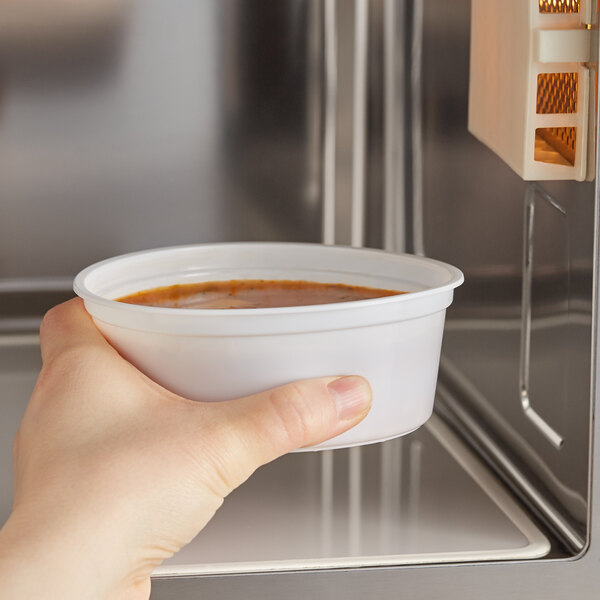 A hand holding a bowl of soup in front of a microwave.