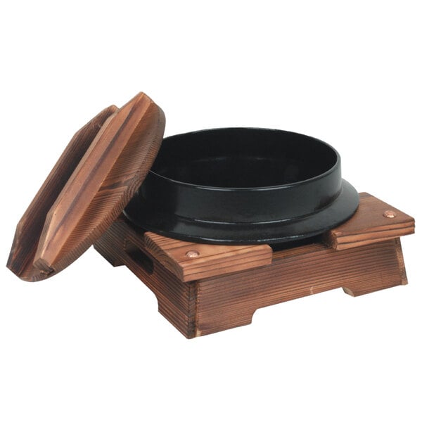 A black cast iron noodle bowl with a lid on a wooden stand.