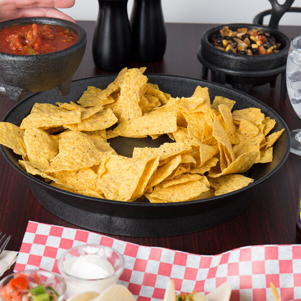 A person holding a bowl of food with black beans and corn on a table with a bowl of chips and salsa.