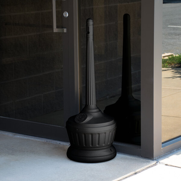 A black pole with a Commercial Zone Smokers' Outpost cigarette receptacle on top outside of a building.