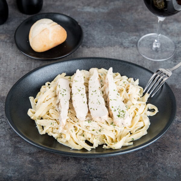 A black Hall China oval platter with chicken pasta and a fork.