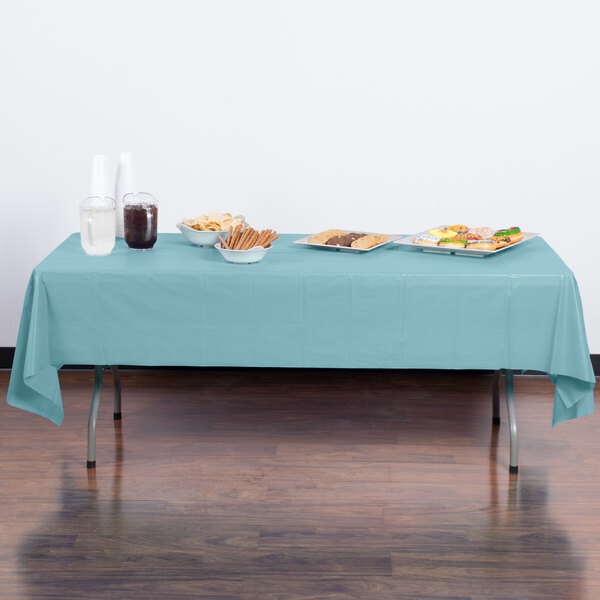 A table with a Creative Converting pastel blue disposable plastic table cover on it with food and plates.