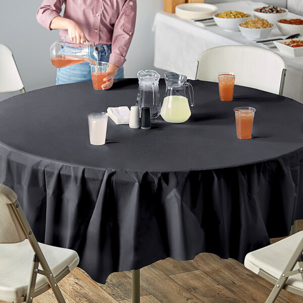 A table with a black Creative Converting tablecloth and glasses of yellow and orange liquid.