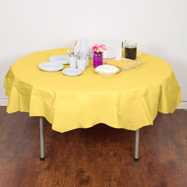 A table with a yellow Creative Converting Mimosa Yellow OctyRound tablecloth, plates, and drinks.
