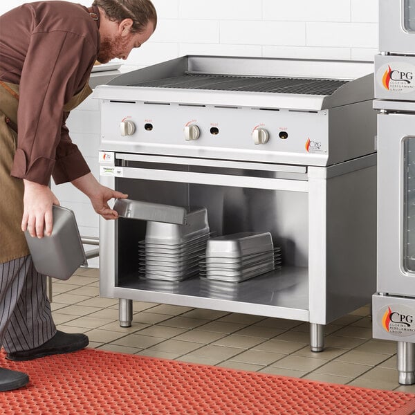 A man using a Regency stainless steel equipment stand to put food in a metal oven.