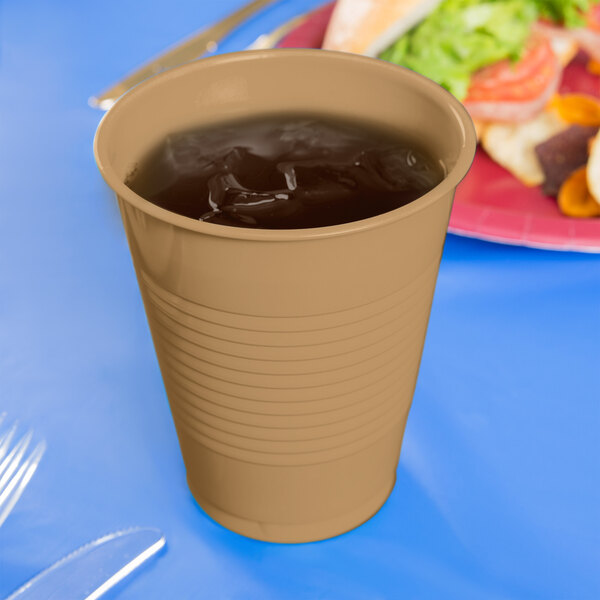 A Creative Converting Glittering Gold plastic cup filled with a cold drink with ice on a table.