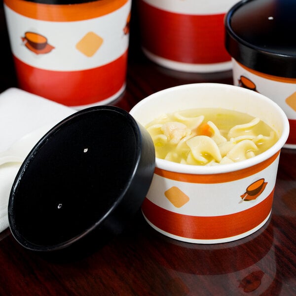 A table with several black and white striped paper soup containers with lids, filled with soup and one with noodles.