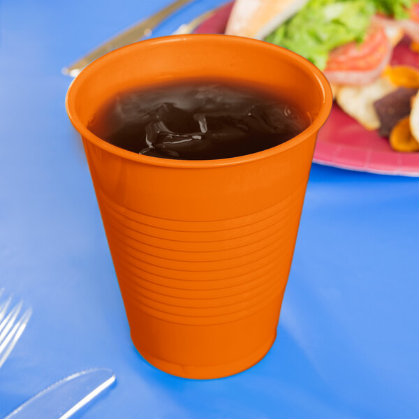 A Creative Converting Sunkissed Orange plastic cup filled with liquid on a blue table