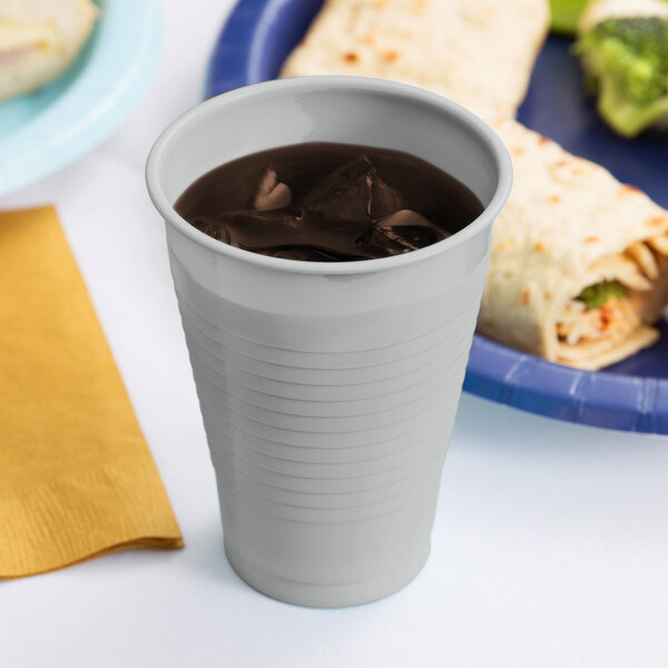 A Shimmering Silver plastic cup filled with a beverage on a table next to a plate of food.