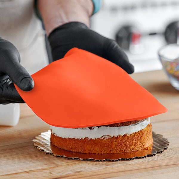 A person wearing black gloves cutting a cake covered in Satin Ice orange vanilla rolled fondant