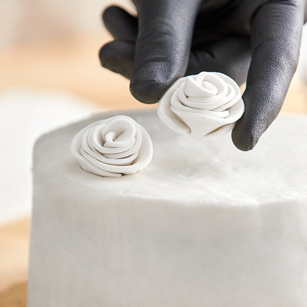 A person's gloved hands using Satin Ice gum paste to add white roses to a cake.