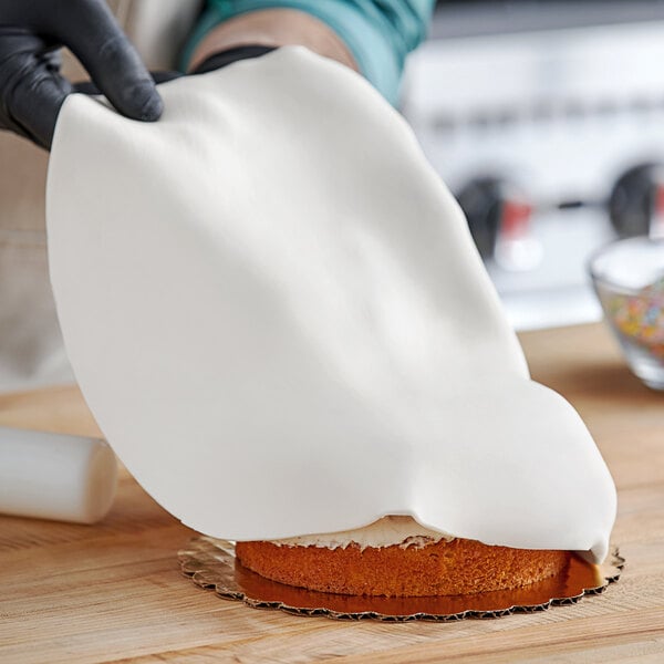 A person holding a white piece of cake with Satin Ice White Vanilla Rolled Fondant over it.