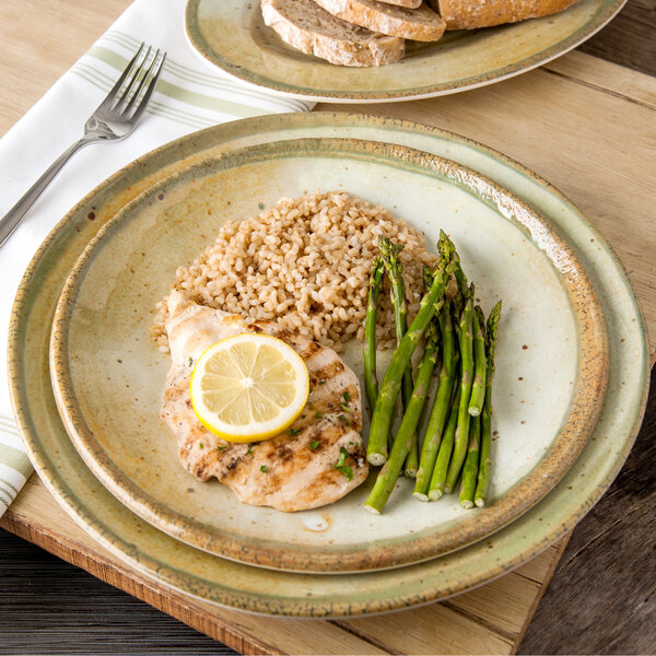 A Carlisle adobe charger plate with a plate of food with rice, asparagus, and chicken with a lemon wedge on top.