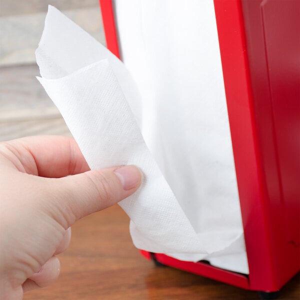 A hand holding a white napkin in front of a red box.