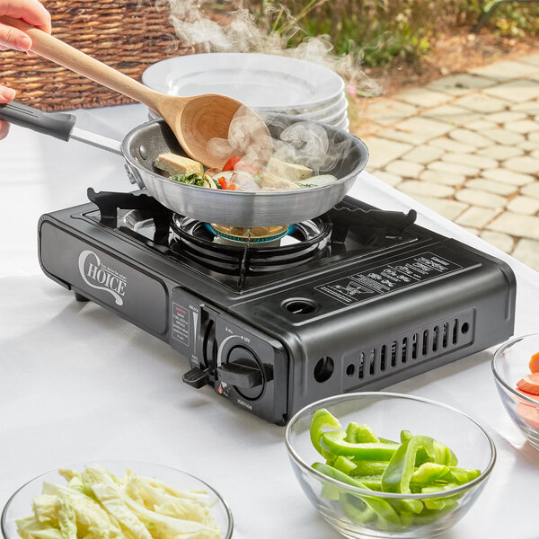 A person using a Choice portable stove to cook food in a pan on a table.