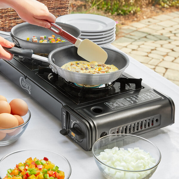 A person using a Choice portable gas stove to cook eggs in a pan.