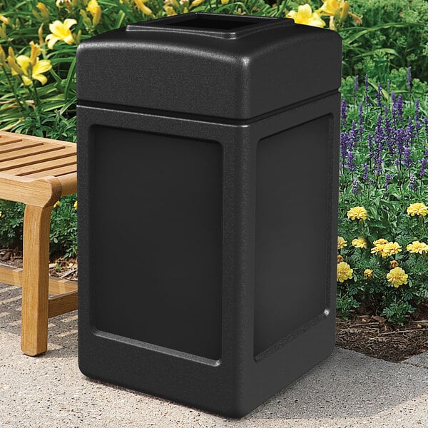 A black rectangular Commercial Zone PolyTec waste container next to a bench.
