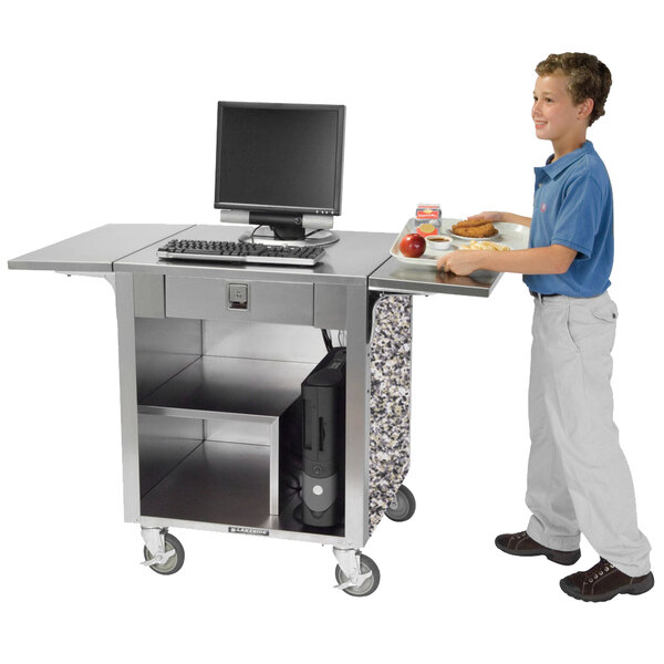 A boy standing next to a Lakeside stainless steel cash register stand with a computer on it.