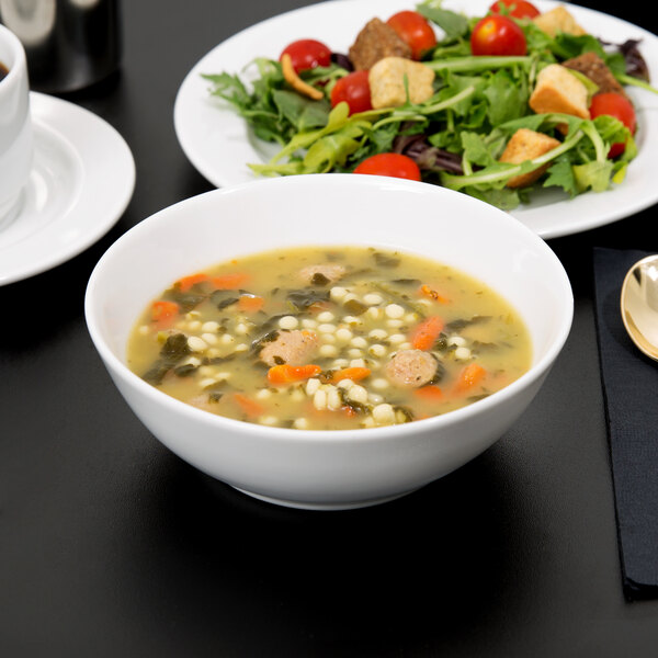 A white Arcoroc porcelain bowl filled with soup and a salad on a table.