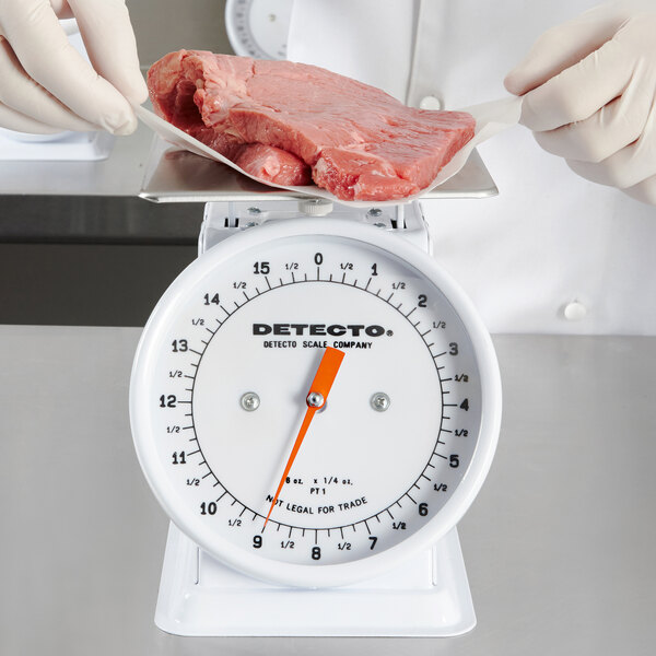 A gloved hand weighing meat on a Cardinal Detecto portion scale.