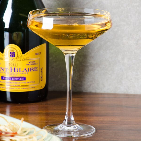 A Chef & Sommelier Cabernet champagne saucer filled with yellow liquid on a table next to a bottle of wine.