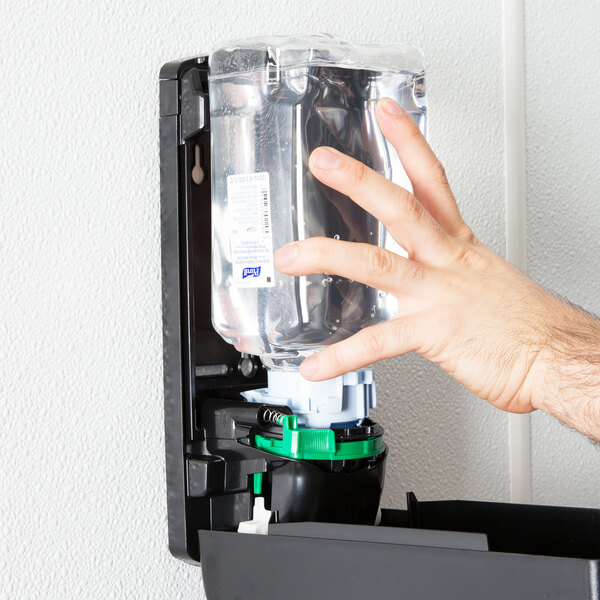 A hand using Purell hand sanitizer in a dispenser.