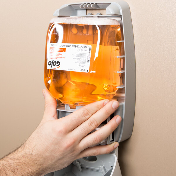A hand holding a bottle of GOJO FMX Orange Blossom antibacterial hand soap.