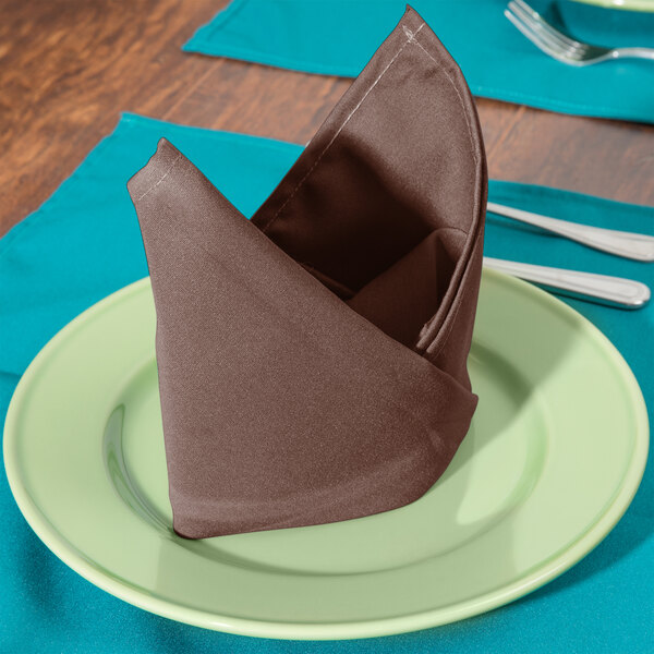 A folded brown Intedge cloth napkin on a plate with a fork and knife.