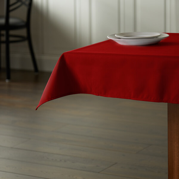 A square red Intedge tablecloth on a table with a plate.
